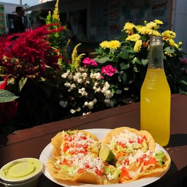 Two El Oasis tostadas with lime, a side of green sauce, and a yellow soda bottle outdoors.