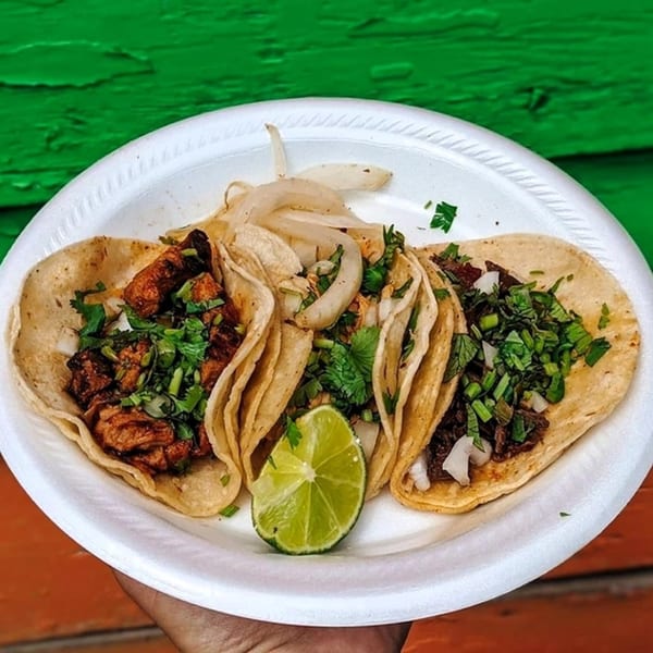 Three El Oasis tacos with meat, cilantro, onions, and a lime wedge on a white plate.